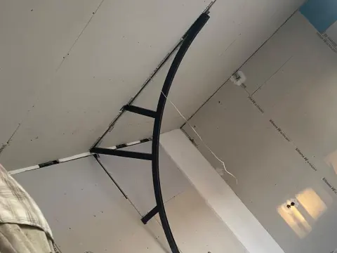 Alçıpan kaplı tavanda kavisli siyah metal iskelet ve ayaklı merdiven, tadilat sürecinde oda