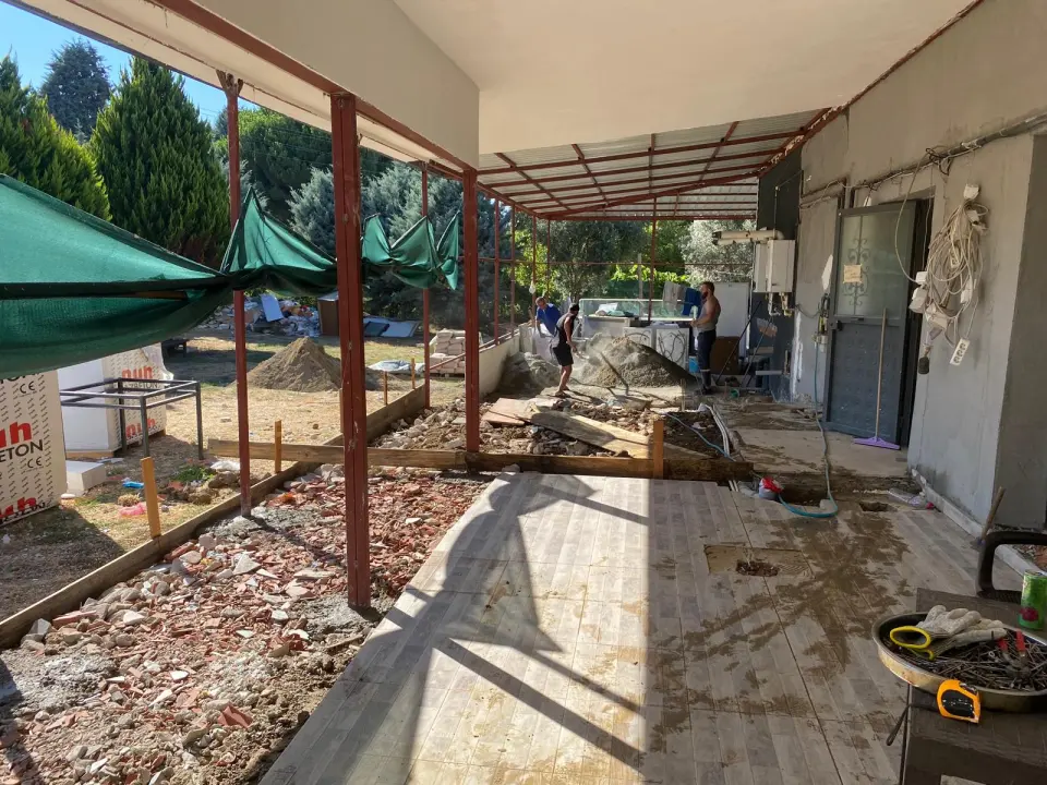 Müstakil ev önünde metal sundurma altında zemin betonu hazırlığı, kalıplar ve çalışan ekip