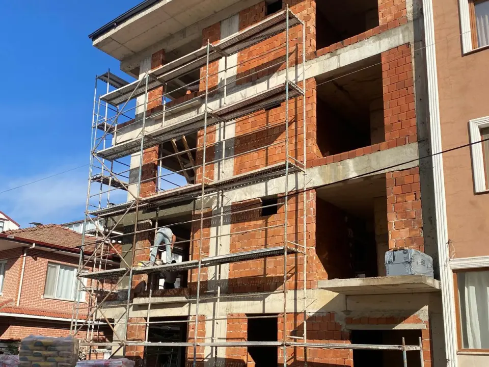 Dört katlı betonarme binada tuğla duvar örme işi, iskele üzerinde ustalar ve önde kum yığını