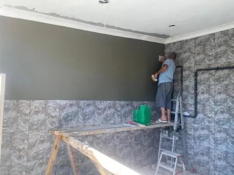 Fayanslı duvarın üst bölümünde usta, iskele üzerinde sıva yüzeyini perdahlıyor