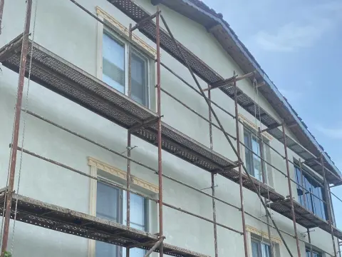 Mantolaması tamamlanmış iki katlı evin dış cephesi; iskele, dekoratif sıva ve pencere çevresinde söve profilleri