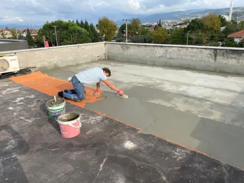 Teras çatıda usta, turuncu donatı filesinin üzerine çimento esaslı yalıtım harcını mala ile yayıyor